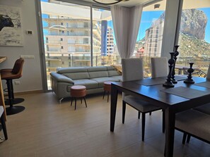A modern living room with a sofa, a dining table, and a view of a cityscape through large windows.