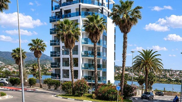 Een meerhoog hotel met balkons, gelegen nabij water en omringd door palmbomen.