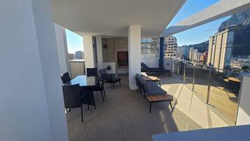 Un balcón moderno con zona de comedor, asientos de descanso y vistas a la ciudad.