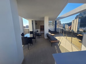 A modern balcony with a dining area, lounge seating, and a view of the cityscape.