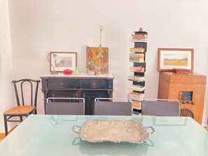 Ein Essbereich mit einem Tisch für zwei Personen, einem schwarzen Korpus mit Dekorationsobjekten und einem hohen Bücherstapel.