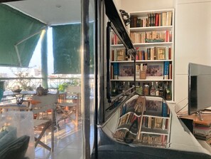 Ein Zimmer mit einem großen Bücherregal, voll mit Büchern und Dekoration, einem Fernseher und Blick durch eine Glastür nach draußen.