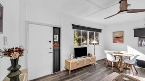 A modern living room with a TV, wooden cabinet, dining table, and chairs. - Camel Rock Cottage - Beauty Point 33 (Wallaga Lake)