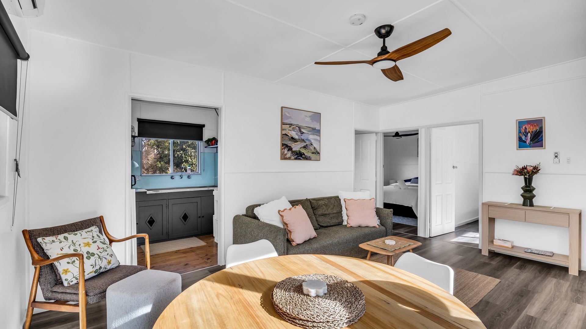 A modern living space with a dining area, kitchen, and a bedroom visible through an open door.