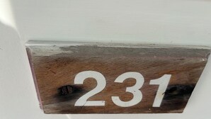 En träskylt med siffran 231, fastsatt på en vit vägg.