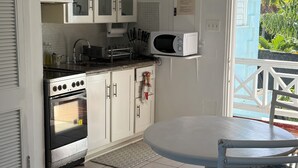 Ett kompakt kök med vita skåp, en mikrovågsugn, en spis och ett litet matbord med en stol.