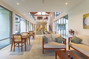 A spacious living area with a high ceiling, a dining table set for four, and a sofa with cushions. - ONA Garden Villa: Double Room with Terrace (Wanchawala)