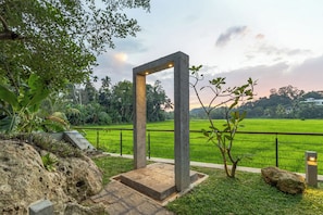 A structure with a concrete base and a metal frame, surrounded by greenery and a view of a green field. - ONA Garden Villa: Double Room with Terrace (Wanchawala)