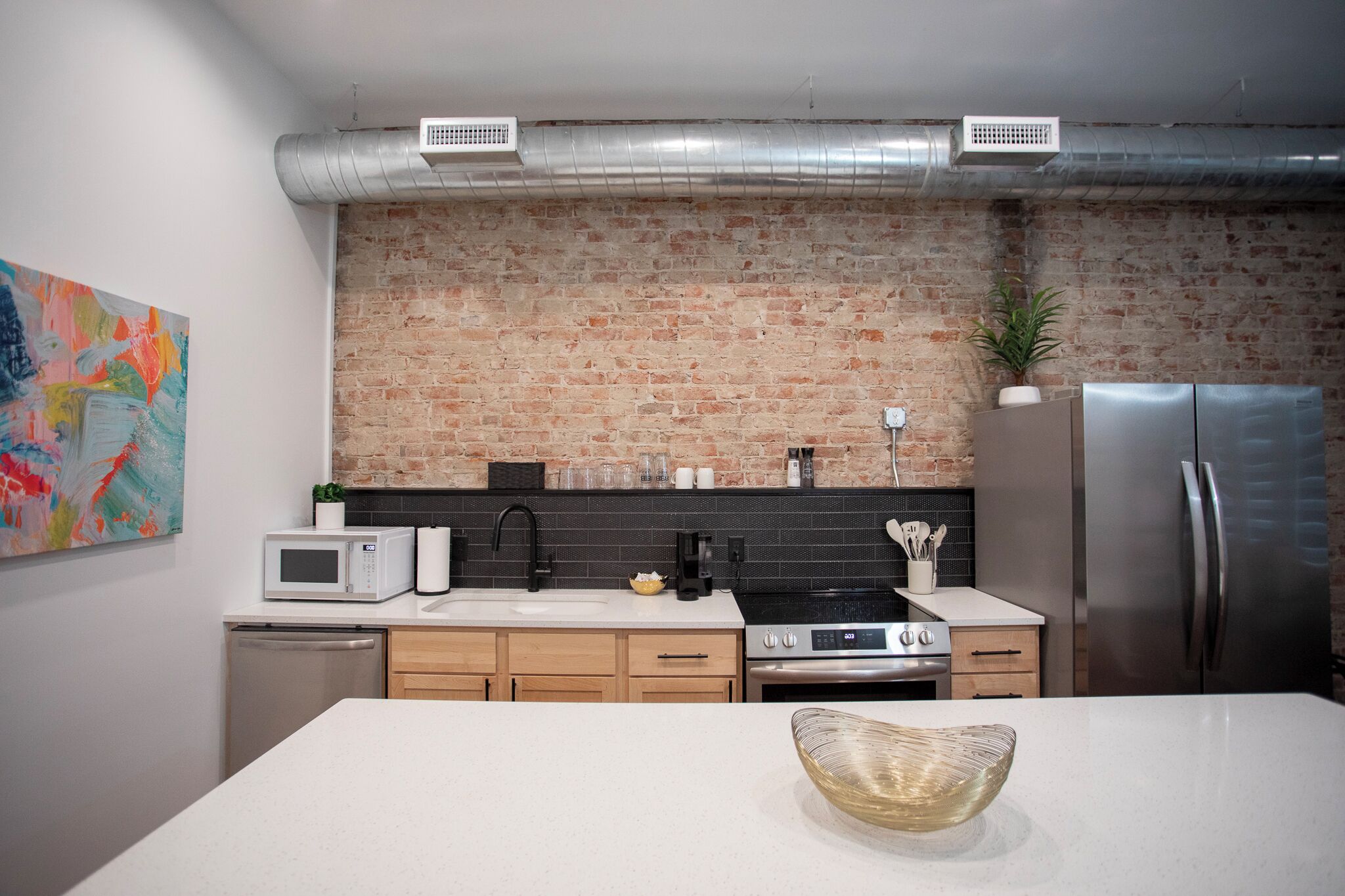 Una cocina moderna con pared de ladrillo, electrodomésticos de acero inoxidable y encimera blanca.