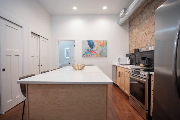 A modern kitchen with a central island, stainless steel appliances, and a colorful abstract painting on the wall.