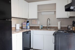 Una cocina con armarios blancos, lavavajillas, estufa y pileta.