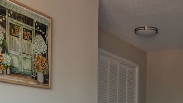 A living room with a grey sofa, a 'welcome home' pillow, a potted plant, and a painting on the wall.