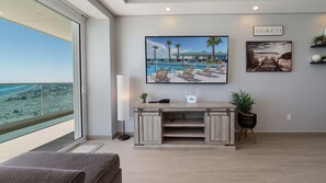 Una habitación con un amplio ventanal con vista a la playa, un escritorio con una computadora portátil, un cuadro de una escena de playa, y un letrero que dice 'Beach'.