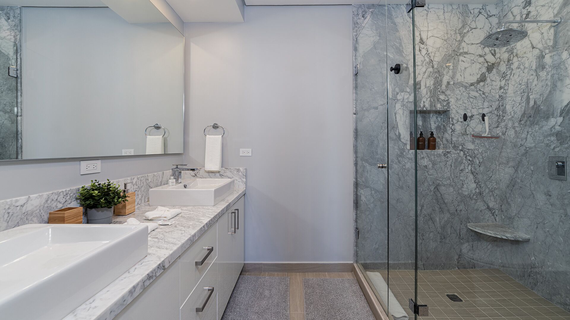 Un bagno moderno con un ampio specchio, due lavabi, una doccia con porta in vetro e pareti in marmo.