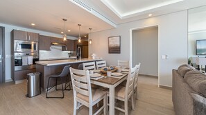 A modern kitchen with built-in appliances, a dining area with a wooden table and chairs, and a living room with a sofa.