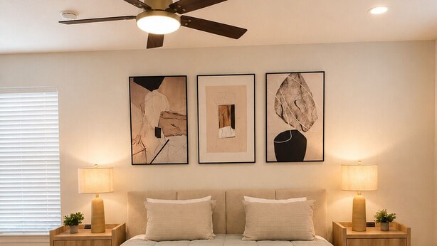A bedroom with a bed, two bedside tables, a ceiling fan, and three framed artworks on the wall.