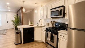 A modern kitchen with white cabinetry, stainless steel appliances, and a wooden floor.
