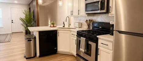 A modern kitchen with white cabinetry, stainless steel appliances, and a wooden floor.