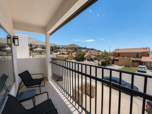 A balcony with a view of a residential area, a stone planter, and a parked car.