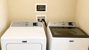 Two Maytag front-loading washing machines in a laundry room with beige walls and a small framed picture on the wall.