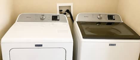 Two Maytag front-loading washing machines in a laundry room with beige walls and a small framed picture on the wall.