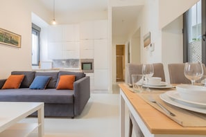 A modern living room with a grey sofa, a dining table set with plates and glasses, and a kitchen area with cabinets and a microwave. - Cozybeautiful Apartment with Wi-Fi and Air Conditioning (Seville)