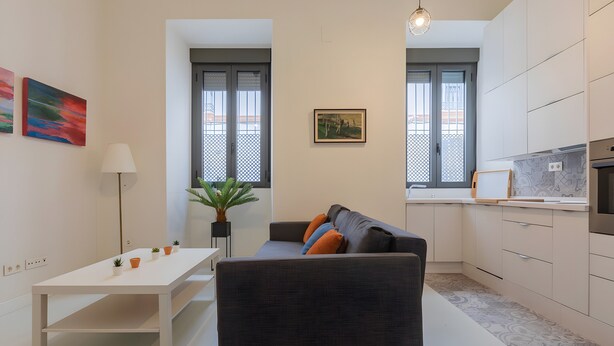 Eine moderne Wohnung mit Essbereich, einer Couch mit Kissen, einer Küche mit Einbauofen und einem großen Fenster mit Blick.