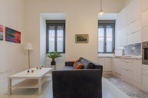 Um apartamento moderno com área de jantar, sofá com almofadas, cozinha com forno embutido e uma janela grande com vista.