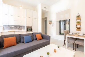 Ein modernes Apartment mit grauem Sofa, einem Esstisch für sechs Personen und einer Küche im Hintergrund.