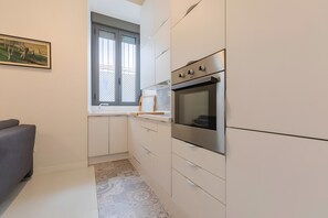 Uma cozinha compacta com forno embutido, uma janela com vista e um sofá cinzento.