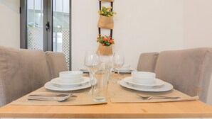 Ein Esstisch ist mit weißen Tellern, Schüsseln, Besteck und Weingläsern gedeckt und wird von beigen, gepolsterten Stühlen begleitet.