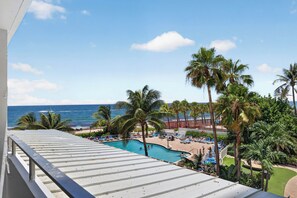 A pool area with lounge chairs and palm trees, overlooking a beach and ocean. - Blue Horizon (Fort Lauderdale)