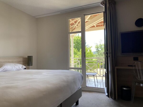 A hotel room with a bed, a desk, a chair, a TV, and a sliding glass door leading to an outdoor area.