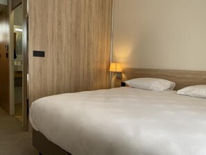 Una habitación de hotel con una cama, una mesita de noche con lámpara y un armario de madera.