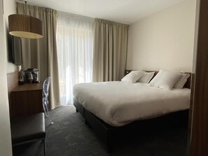 A hotel room with a bed, a desk with a lamp, and a window with curtains. - Domaine de la Reynaude (Aurons)