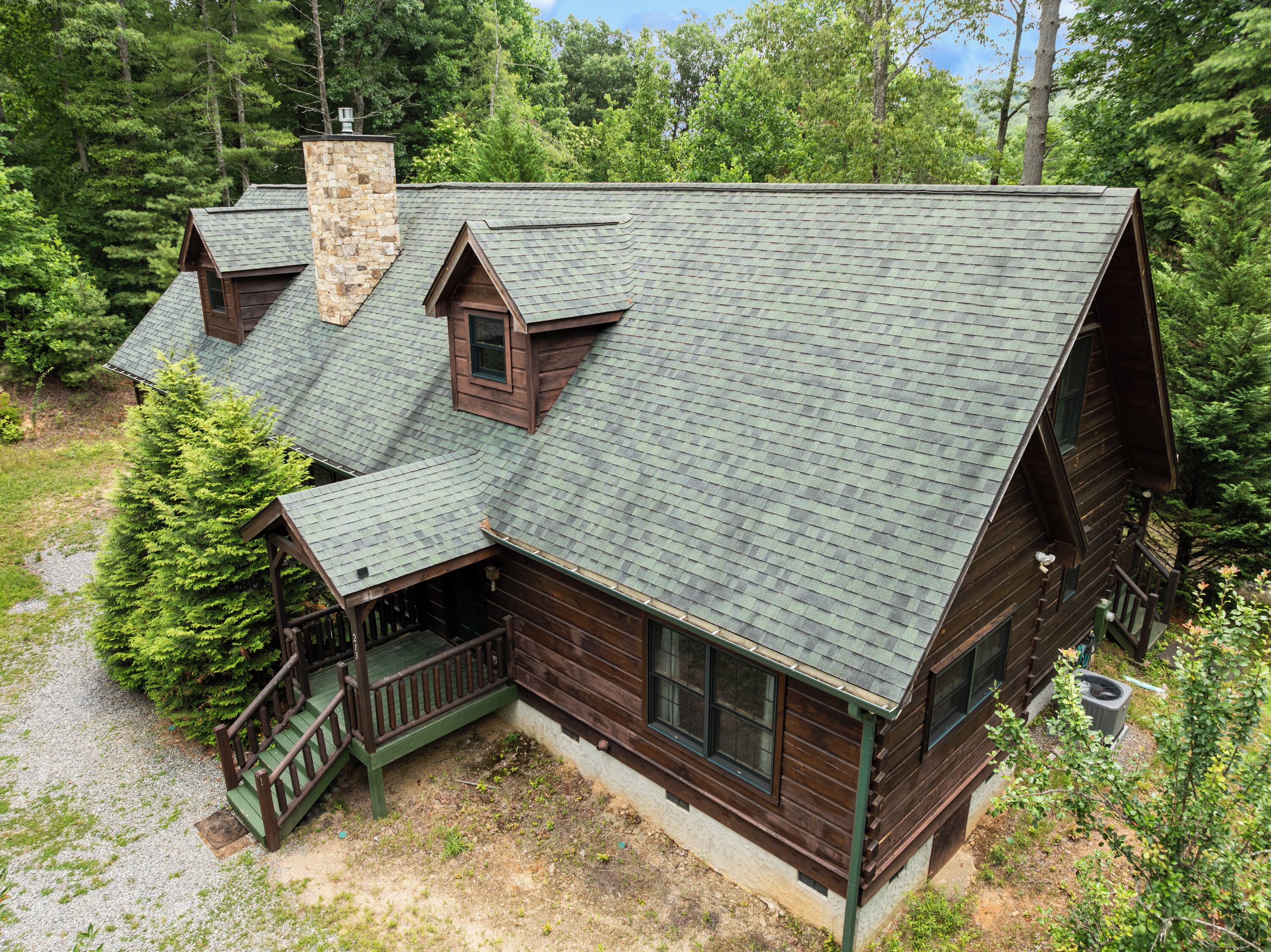 A cabin with a steeply pitched roof, a chimney, and a porch with a railing.