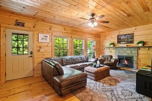 A log cabin interior with a leather sofa, a fireplace, and a ceiling fan.