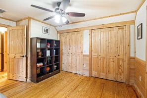 Ein Zimmer mit Holzdielen, einem Deckenventilator, einem Bücherregal und Holztüren.