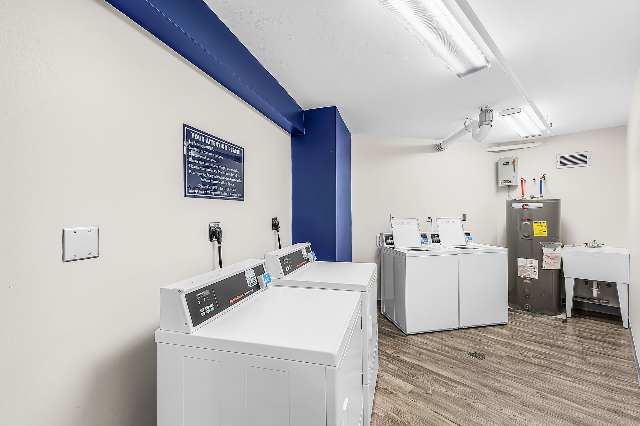 A laundry facility with multiple washing machines, a blue accent wall, and a sign with usage instructions.