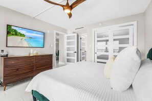 Un dormitorio con cama, cómoda, televisor y ventilador de techo.