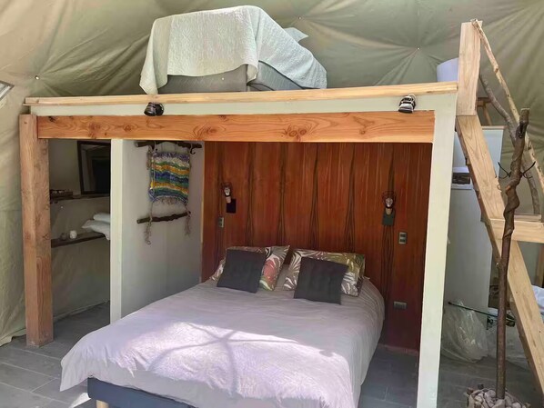 A tented room with a bed, wooden walls, a hanging tapestry, and a ladder.