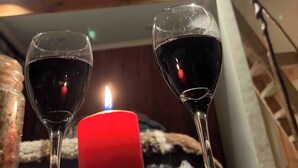 Two wine glasses on a table with a lit candle, a geometric ceiling light, and a partial view of a bed with a blanket. - Domos Palguin (Palguin Alto)