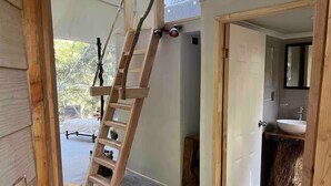 A wooden ladder leaning against a wall in a room with a tiled floor, a door leading to a bathroom with a sink, and a view of the outdoors. - Domos Palguin (Palguin Alto)
