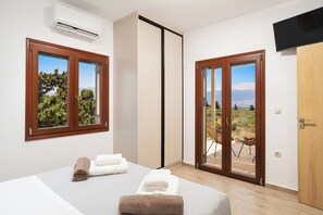 A bedroom with a bed, two windows, an air conditioning unit, and a sliding door leading to an outdoor area. - Peaceful Luxury Villa with Private Pool See View and Mountain View (Χανιά)