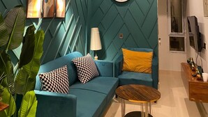 A modern living room with a teal accent wall, a large wall clock, a ceiling fan, and a coffee table. - Lovely 1-bedroom apartment with AC in vibrant Karachi (Karachi)