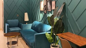 A modern living room with a teal accent wall, a ceiling fan, a blue sofa, a wooden coffee table, a brown leather chair, and a potted plant. - Lovely 1-bedroom apartment with AC in vibrant Karachi (Karachi)