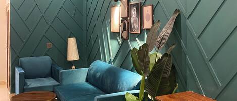 A modern living room with a teal accent wall, a ceiling fan, a blue sofa, a wooden coffee table, a brown leather chair, and a potted plant.