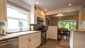 A kitchen with white cabinets, a microwave, an oven, and a coffee maker. There is a dining area with a table and chairs visible through an open doorway. - 10-Min Walk to Downtown & Lake • 10-Min Drive to Schweitzer Base (Sandpoint)