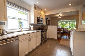A kitchen with white cabinets, a microwave, an oven, and a coffee maker. There is a dining area with a table and chairs visible through an open doorway. - 10-Min Walk to Downtown & Lake • 10-Min Drive to Schweitzer Base (Sandpoint)