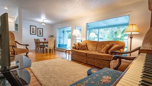 A living room with a piano, a sofa, a dining table with chairs, and large windows. - 10-Min Walk to Downtown & Lake • 10-Min Drive to Schweitzer Base (Sandpoint)